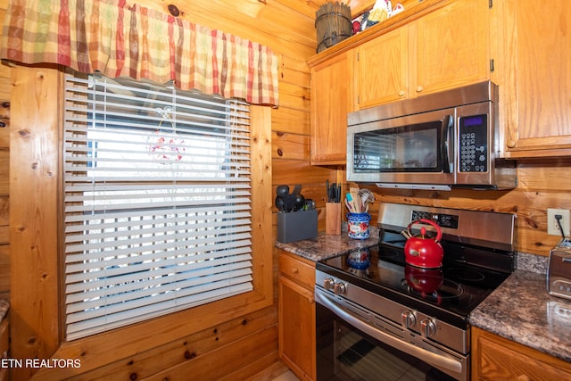 kitchen featuring appliances with stainless steel finishes, wood walls, and dark stone countertops