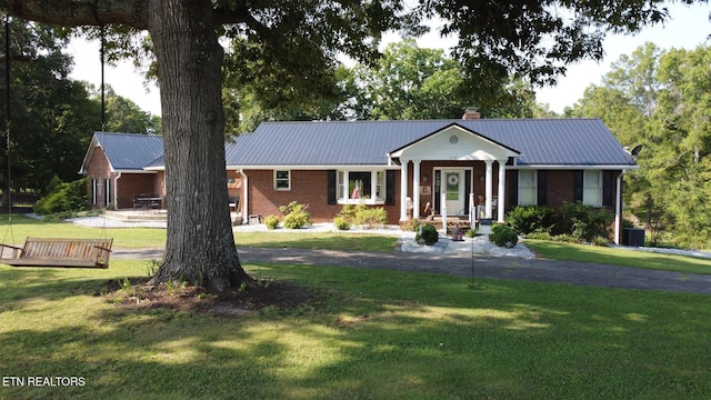 view of front of house with metal roof, brick siding, a chimney, and a front yard