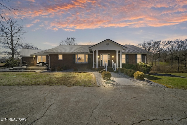 view of front of home with metal roof, driveway, brick siding, and a standing seam roof