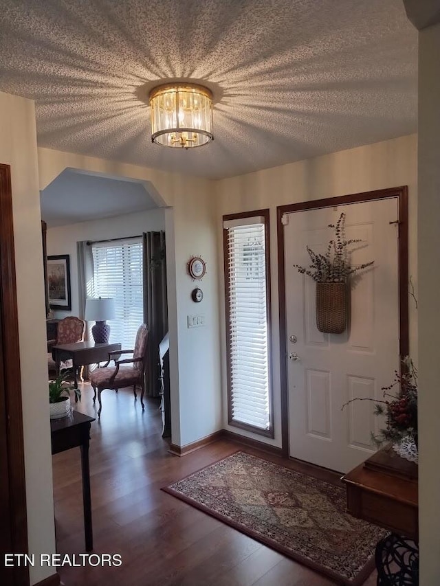 entrance foyer featuring baseboards, a textured ceiling, an inviting chandelier, and wood finished floors