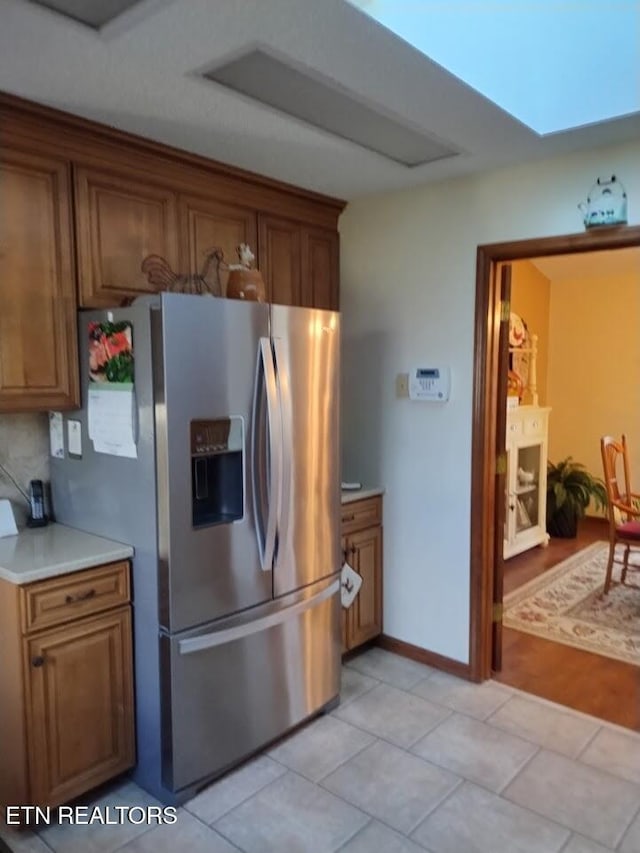 kitchen featuring brown cabinetry, light countertops, stainless steel refrigerator with ice dispenser, and light tile patterned floors