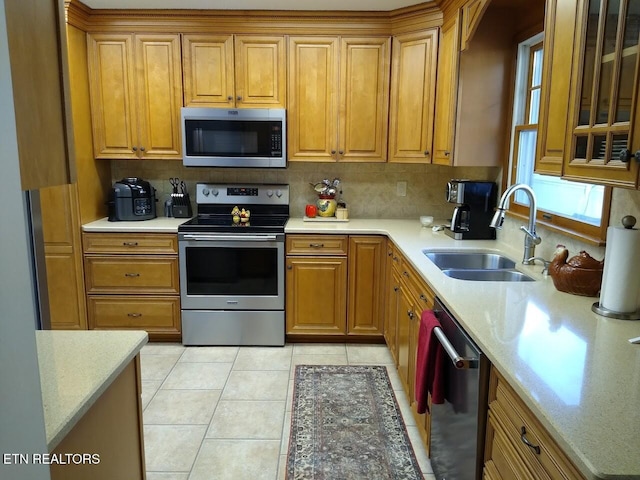 kitchen featuring light tile patterned floors, brown cabinetry, decorative backsplash, stainless steel appliances, and a sink