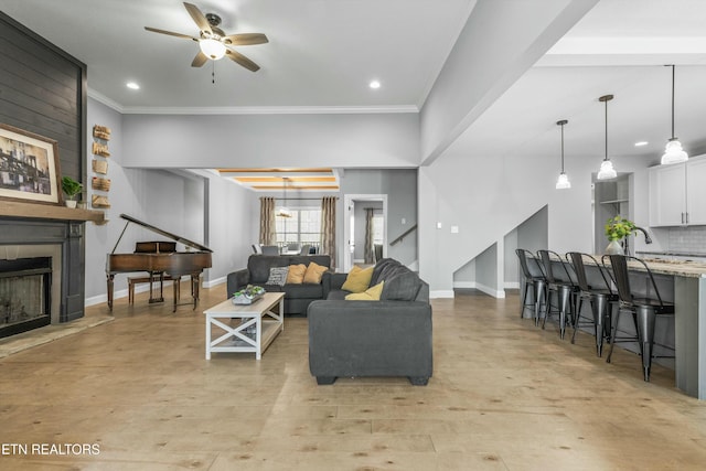 living room with a large fireplace, a ceiling fan, baseboards, light wood-style floors, and ornamental molding