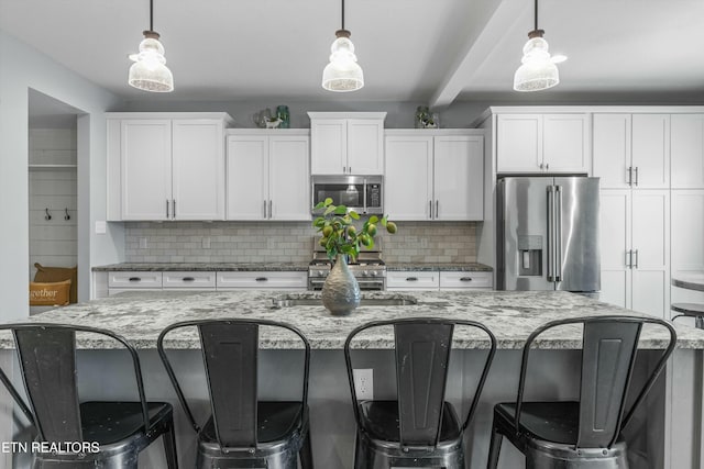 kitchen with stainless steel appliances, a sink, hanging light fixtures, and an island with sink