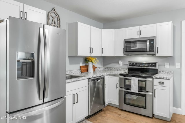 kitchen with light wood finished floors, white cabinetry, stainless steel appliances, and light stone counters