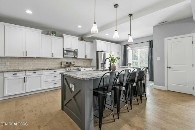 kitchen with a kitchen island with sink, light wood-style flooring, white cabinetry, appliances with stainless steel finishes, and tasteful backsplash