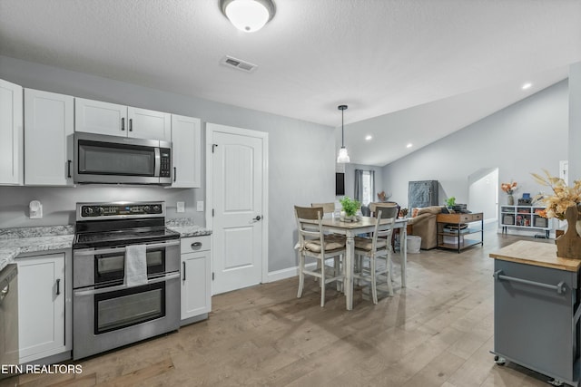 kitchen featuring stainless steel appliances, white cabinetry, visible vents, vaulted ceiling, and light wood-style floors