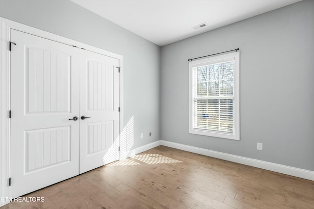 unfurnished bedroom with a closet, wood-type flooring, visible vents, and baseboards