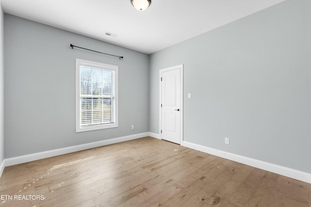 empty room featuring wood-type flooring, visible vents, and baseboards