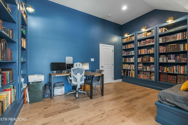 office area featuring vaulted ceiling, built in shelves, wood finished floors, and bookshelves