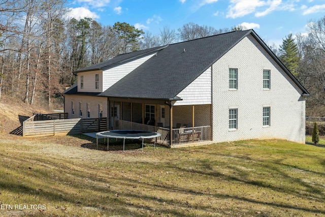 back of property with a trampoline, fence, a lawn, and brick siding