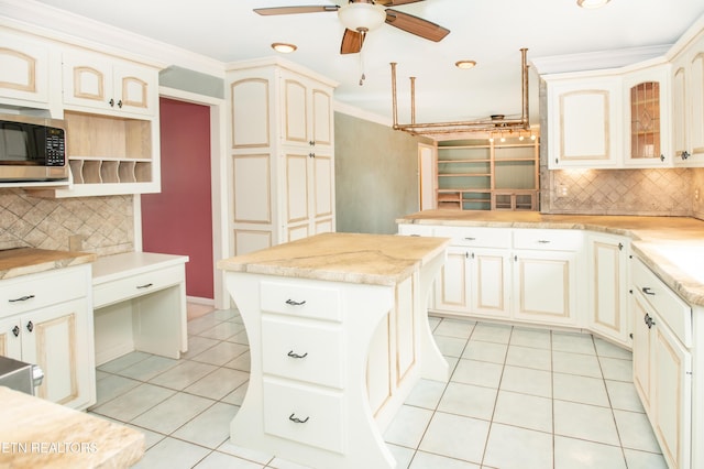 kitchen with light tile patterned floors, ceiling fan, crown molding, stainless steel microwave, and backsplash