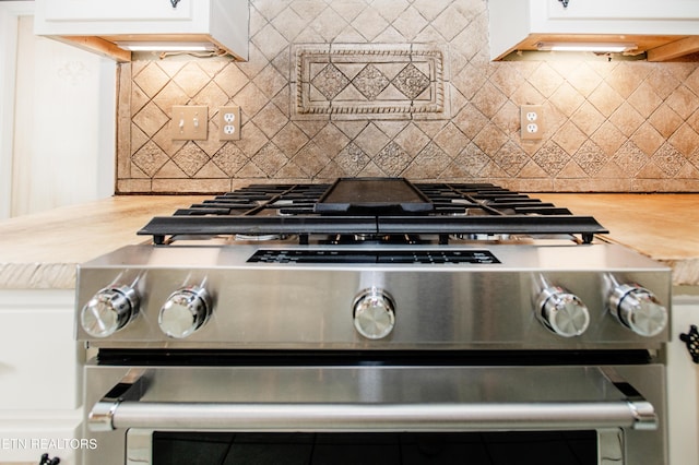 kitchen featuring decorative backsplash, gas stove, and white cabinetry