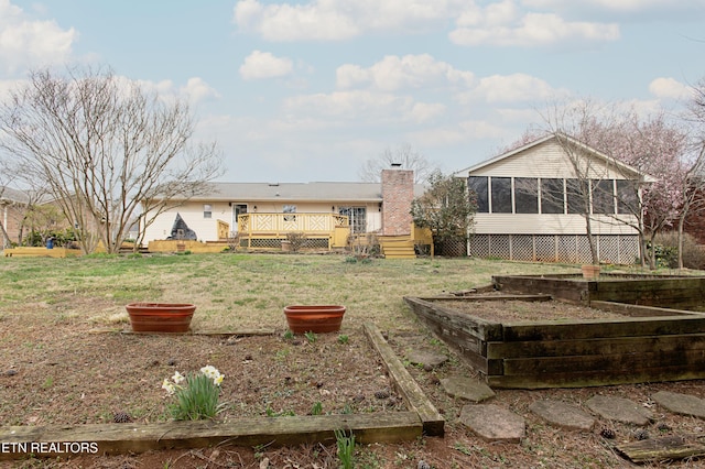 back of property featuring a wooden deck, a lawn, a chimney, a sunroom, and a vegetable garden