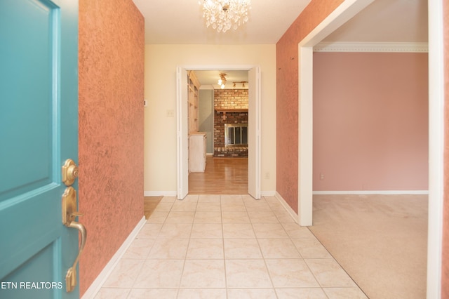 corridor with light carpet, ornamental molding, an inviting chandelier, light tile patterned floors, and baseboards