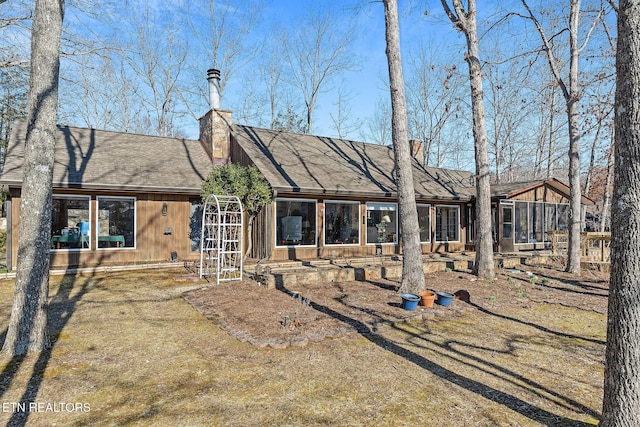 rear view of house with roof with shingles, a chimney, and a sunroom