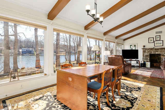 dining area featuring lofted ceiling with beams, a stone fireplace, a water view, visible vents, and an inviting chandelier