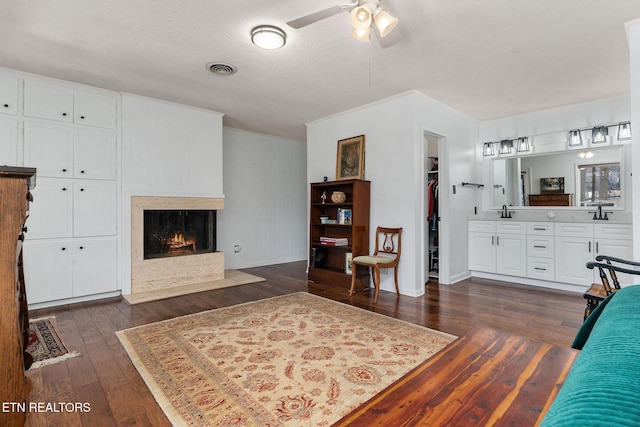 living area with dark wood finished floors, visible vents, a ceiling fan, a textured ceiling, and a warm lit fireplace