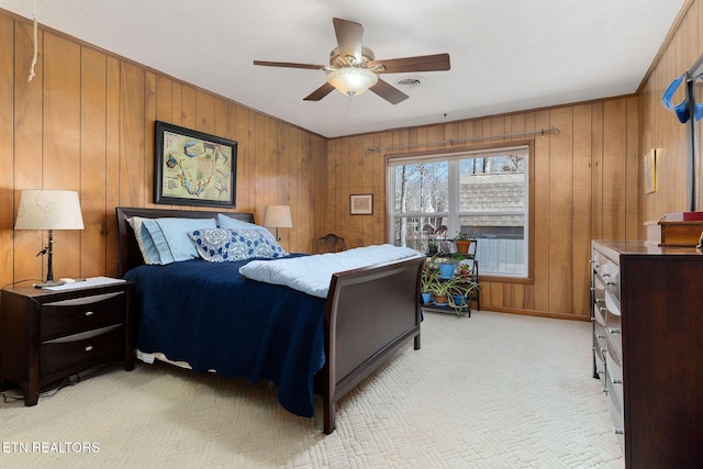 bedroom featuring visible vents, a ceiling fan, light carpet, wooden walls, and baseboards