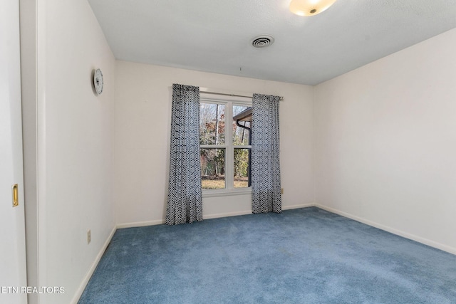 spare room featuring dark carpet, visible vents, and baseboards