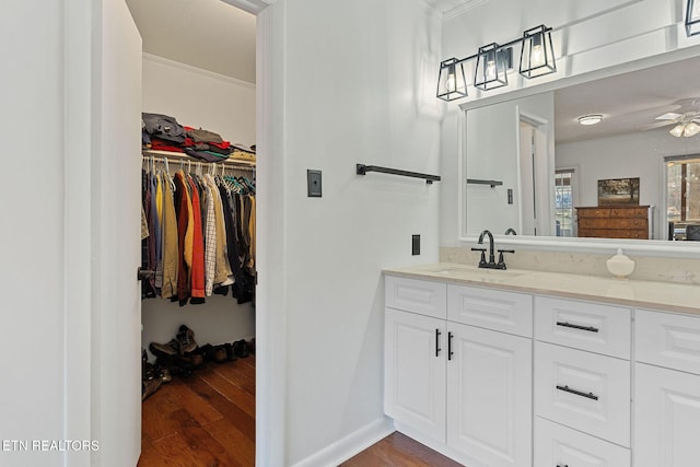 bathroom with ceiling fan, ornamental molding, wood finished floors, a walk in closet, and vanity