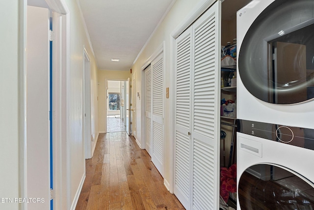 clothes washing area with stacked washer and clothes dryer, crown molding, light wood-style flooring, laundry area, and baseboards