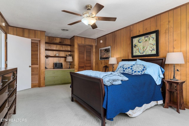 bedroom with ceiling fan, wood walls, and light colored carpet