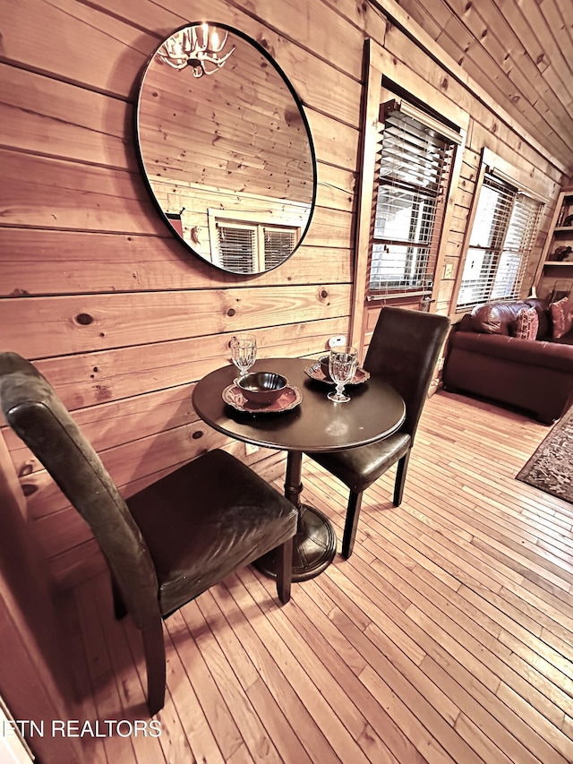 dining space with a chandelier, wood ceiling, wooden walls, and light wood finished floors