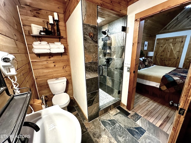 ensuite bathroom featuring a sink, wood walls, a shower stall, and stone tile flooring