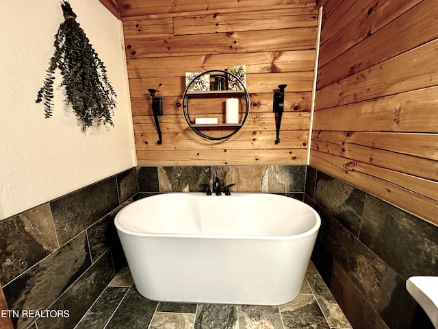 bathroom with a freestanding bath, stone finish floor, and wooden walls