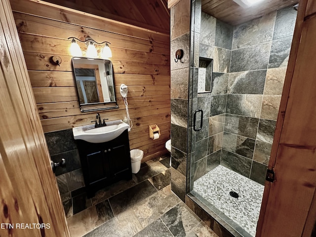 bathroom featuring toilet, stone tile flooring, vanity, wood walls, and a shower stall