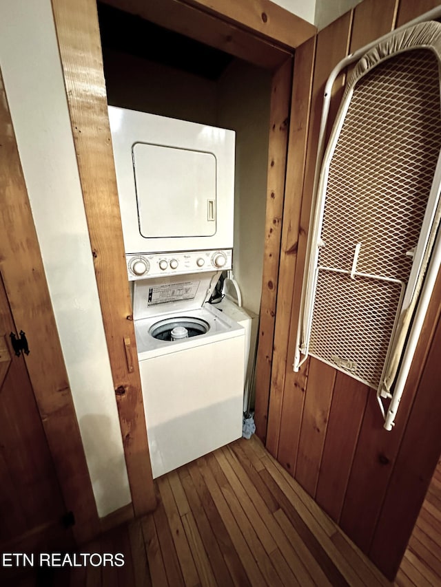 clothes washing area with laundry area, wood-type flooring, and stacked washing maching and dryer