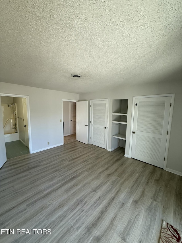 7000 Big Horn Dr Unit A-3, Crossville, TN 38572 - unfurnished bedroom featuring baseboards, two closets, a textured ceiling, and wood finished floors