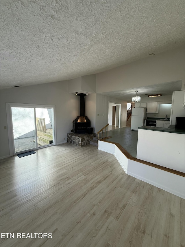 7000 Big Horn Dr Unit A-3, Crossville, TN 38572 - unfurnished living room featuring lofted ceiling, an inviting chandelier, light wood-style floors, a wood stove, and a textured ceiling