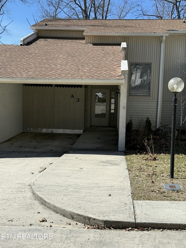 property entrance with a carport, a shingled roof, and driveway