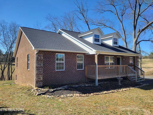 view of front facade featuring a shingled roof, covered porch, brick siding, and a front lawn