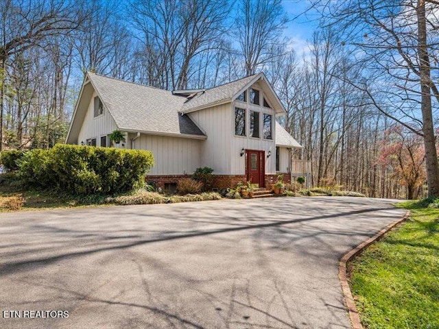 view of side of home featuring brick siding, driveway, and a shingled roof