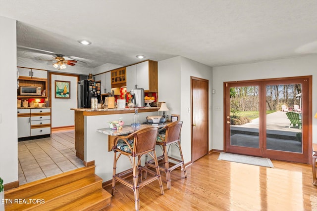 kitchen featuring a ceiling fan, stainless steel microwave, freestanding refrigerator, a peninsula, and light wood finished floors