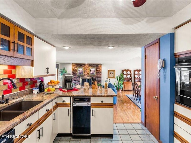 kitchen with a peninsula, black appliances, a textured ceiling, and a sink