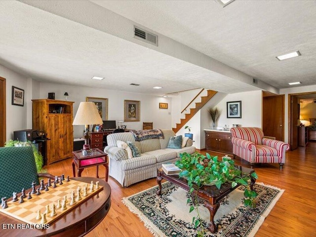 living room with visible vents, a textured ceiling, stairs, and wood finished floors