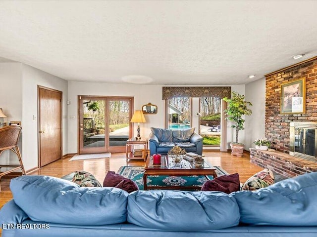 living room featuring a fireplace, a textured ceiling, baseboards, and wood finished floors