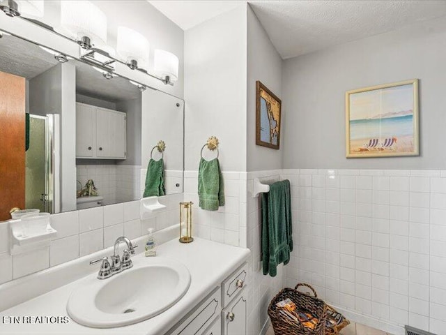 full bathroom with a stall shower, a textured ceiling, tile walls, wainscoting, and vanity