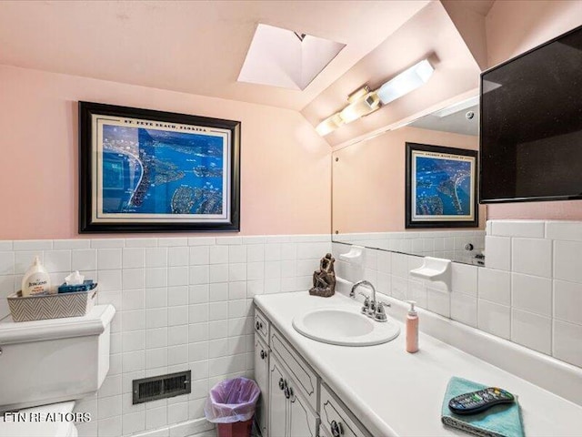 bathroom with visible vents, toilet, tile walls, wainscoting, and vanity