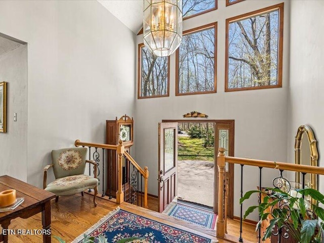 foyer entrance featuring a notable chandelier, a healthy amount of sunlight, wood finished floors, and high vaulted ceiling