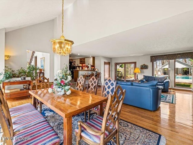 dining area with a notable chandelier, lofted ceiling, and wood finished floors