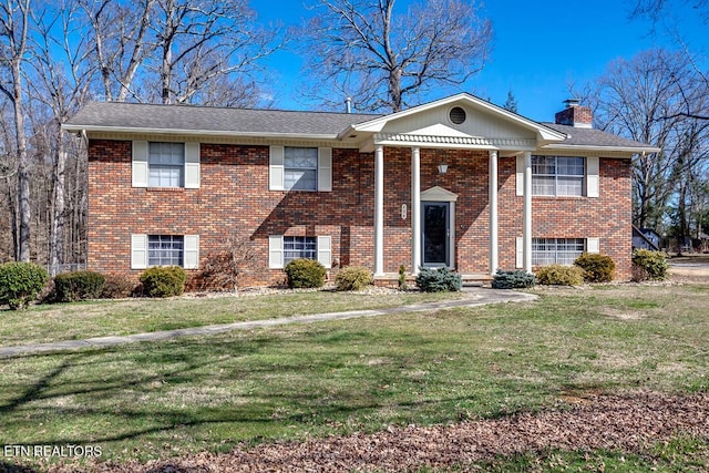 view of front of house featuring a chimney, a front lawn, and brick siding