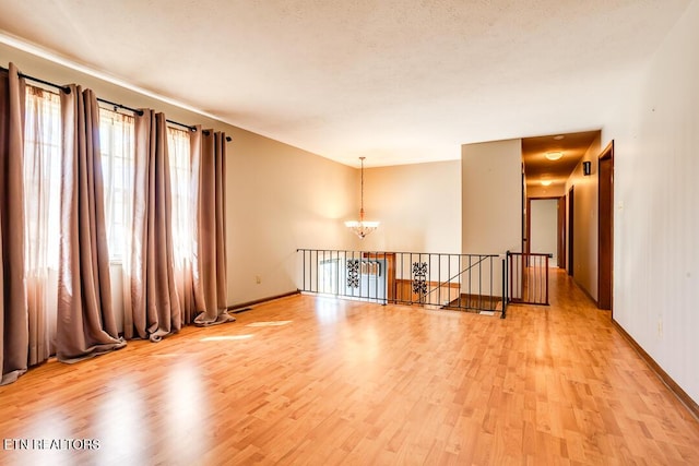 empty room featuring an inviting chandelier, baseboards, light wood finished floors, and a textured ceiling