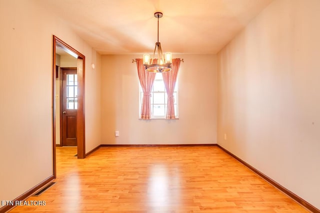 spare room with a chandelier, light wood-type flooring, visible vents, and baseboards