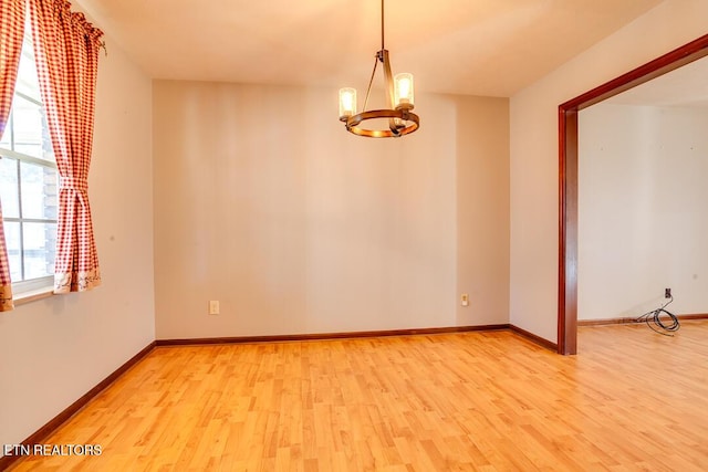 empty room with light wood-style floors, baseboards, and a notable chandelier