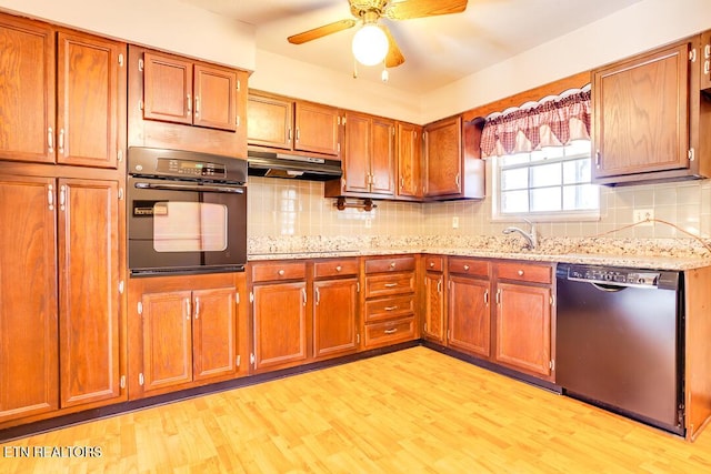 kitchen with light wood-style floors, brown cabinetry, under cabinet range hood, and black appliances